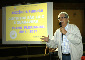 Foto do secretário de planejamento, orçamento e tecnologia Daniel Pelisson, tomando a palavra na audiência, ao fundo apresentação da audiência em vídeoprojetor